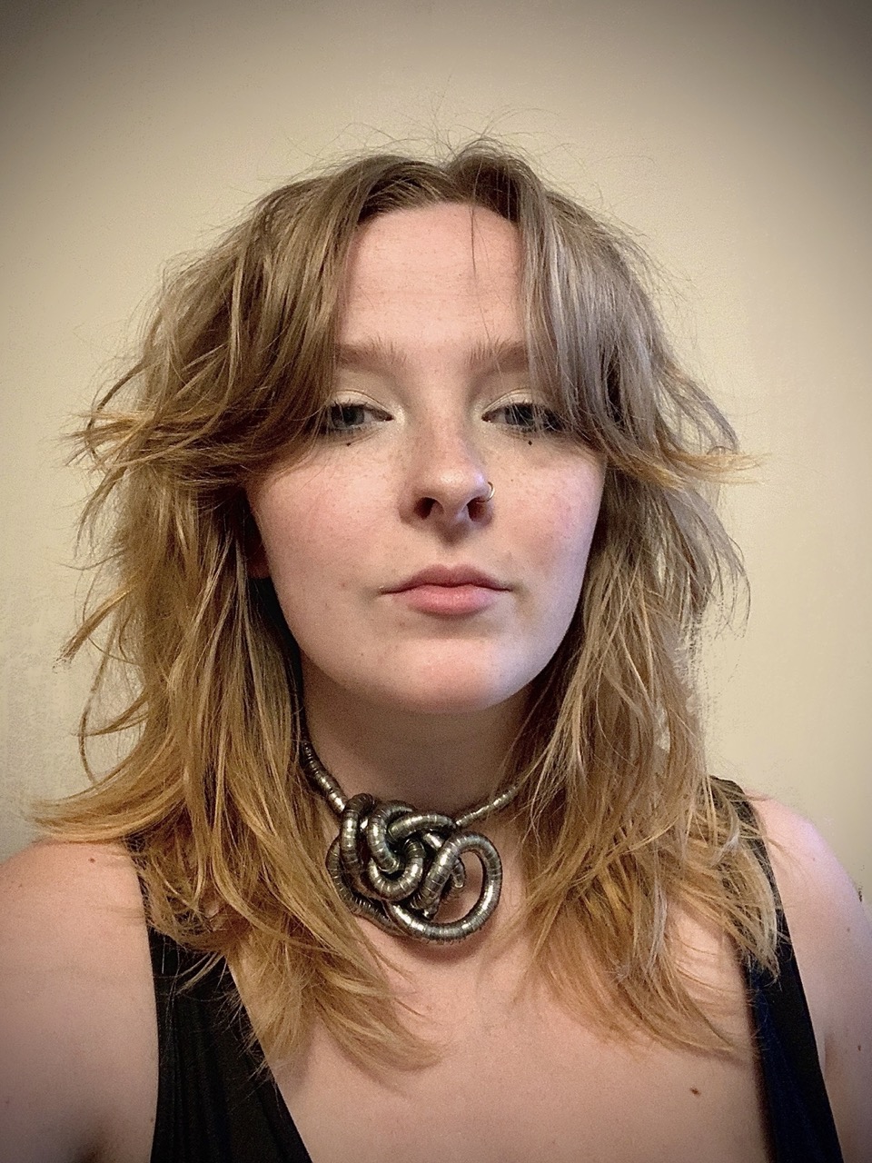 Carlyn's Headshot - they are posing with their chin slightly raised and looking at the camera a neutral background behind them